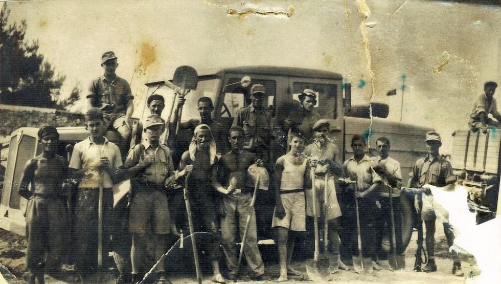 Συνεργείο καταναγκαστικής εργασίας σε ολιγόλεπτη διακοπή. Ενοπλοι φρουροί επιτηρούν τους ξυπόλητους νεαρούς ομήρους. Δεύτερος εξ αριστερών ο Ευάγγελος Θεοδωρόπουλος (1926-1999) από τις Μηλιές Πηλίου
